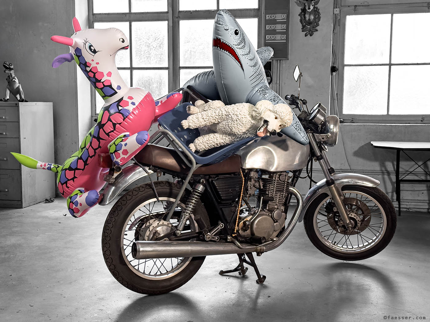 Two large inflatable animals and a white poodle piled up on a vintage motorcycle as a spontaneous ad hoc sculpture at studio Zurich; works of art as figurative sculptures; artist Roland Faesser, sculptor and painter 2025